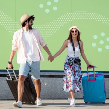Couple in summer clothing holding hands while pulling rolling luggages